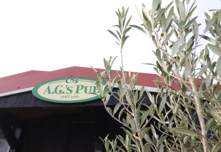 Skiltet til A.G.'s Pub ved luksus safaritelt på Ameland, Holland, delvist skjult af grønne grene.