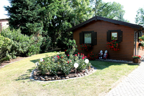 Gezellige houten chalet met bloemenperken en tuinbeeldjes bij By Ostseebad Rerik op een zonnige dag.