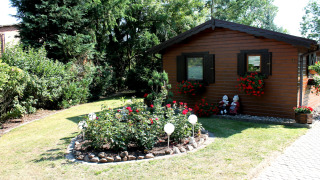 Gezellige houten chalet met bloemenperken en tuinbeeldjes bij By Ostseebad Rerik op een zonnige dag.