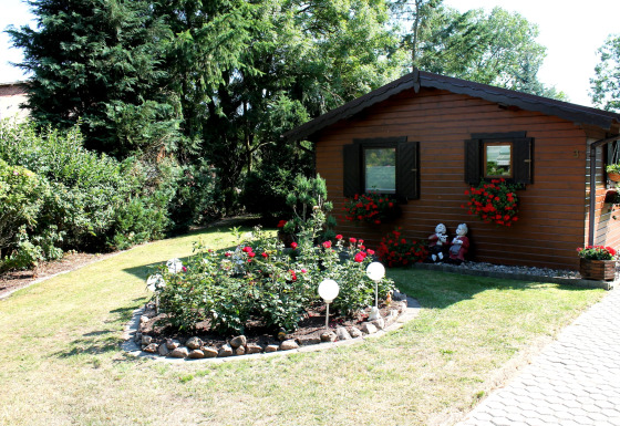 Gezellige houten chalet met bloemenperken en tuinbeeldjes bij By Ostseebad Rerik op een zonnige dag.