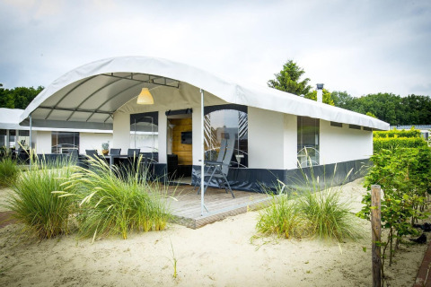 Safari tent at Recreation Park Duinhoeve 7, featuring a covered porch with sand and surrounding greenery.