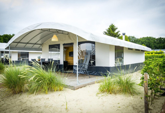 Safari telt ved Recreation park Duinhoeve 7 med overdækket terrasse og sand omgivet af grønne buske.
