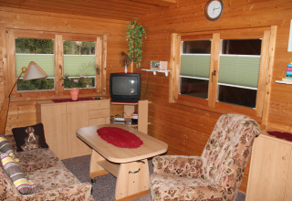 Soggiorno accogliente con pareti in legno, poltrone floreali e TV vintage nel chalet By Ostseebad Rerik in Germania.