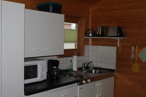 Piccola cucina in una baita di legno vicino a Ostseebad Rerik, Germania, con mobili bianchi e elettrodomestici.