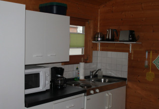 Piccola cucina in una baita di legno vicino a Ostseebad Rerik, Germania, con mobili bianchi e elettrodomestici.