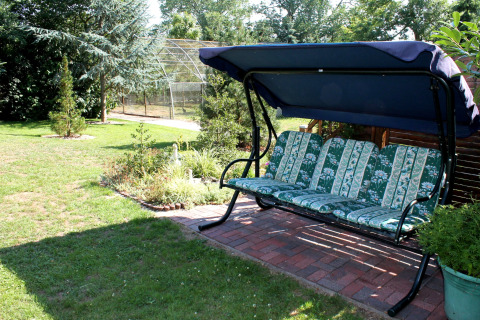 Dondolo da giardino con cuscini floreali e tettoia blu vicino alla cabina ‘By Ostseebad Rerik’, Germania.