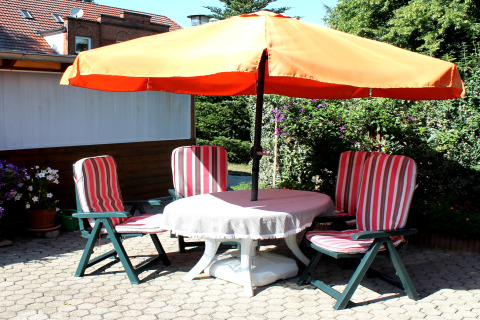 Patio presso una cabina a Ostseebad Rerik, Germania, con ombrellone arancione e quattro sedie a righe.