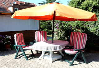 Patio presso una cabina a Ostseebad Rerik, Germania, con ombrellone arancione e quattro sedie a righe.