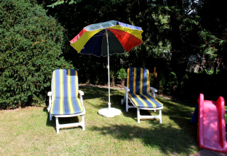 Twee ligzetels met strepen en een kleurrijke parasol in de tuin bij de chalet By Ostseebad Rerik in Duitsland.