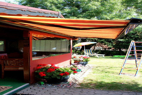 Terrazza soleggiata di una baita vicino a Ostseebad Rerik, Germania, con tenda a righe, fiori e area giochi.