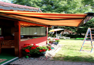 Terrazza soleggiata di una baita vicino a Ostseebad Rerik, Germania, con tenda a righe, fiori e area giochi.