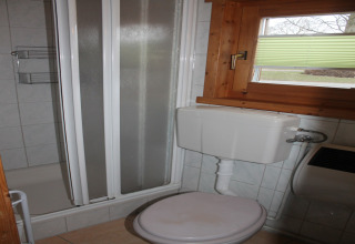 Kleine badkamer met toilet, douche en houten raam in een chalet bij Ostseebad Rerik, Duitsland.