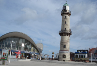 Afbeelding van vuurtoren en modern gebouw aan de kustlijn van Ostseebad Rerik, Duitsland op een zonnige dag.
