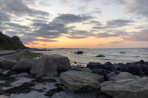 Zonsondergang aan een rotsachtig strand bij Ostseebad Rerik, Duitsland, met golven en bewolkte lucht.