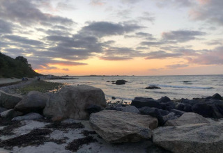 Tramonto su una spiaggia rocciosa vicino a Ostseebad Rerik, Germania, con onde e cielo nuvoloso.