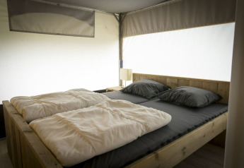 Cama doble cómoda con estructura de madera y ropa de cama oscura en una tienda safari en Duinhoeve.
