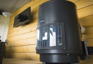 Poêle noir Pelgrim dans une tente safari Duinhoeve 7, avec mur en bois et télévision en arrière-plan.