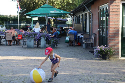 En pige leger med en strandbold foran en udendørs café på Duinhoeve 7, en safaritelt i Holland.