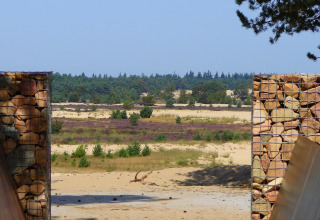 View from a safari tent at Recreation park Duinhoeve 7, Netherlands, showing sand, stones and fields.