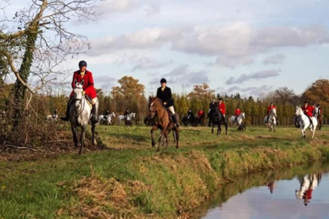 Jinetes con chaquetas rojas y negras cabalgan junto a un estanque en el parque Duinhoeve 7, Países Bajos.