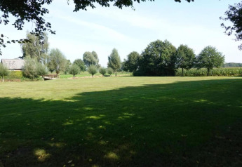 Vista de un campo verde, árboles y una casa pequeña en el parque recreativo Duinhoeve, Países Bajos.