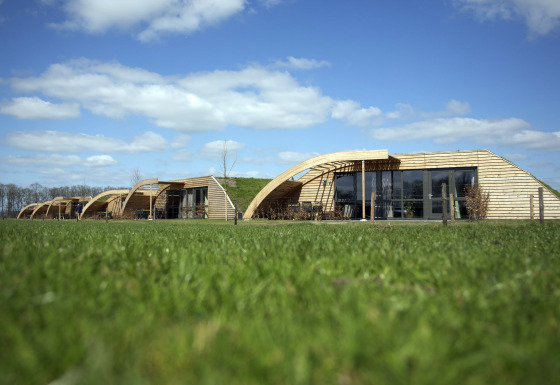 Foto af moderne lodge-bygninger med træfacade og buede linjer under en klar blå himmel og grønne marker.
