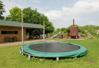 Area esterna di un rifugio con tappeto elastico interrato, scivolo da gioco e prato verde curato.