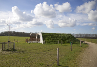 Et moderne græsdækket lodge-bygning i det åbne landskab under en blå himmel med skyer.