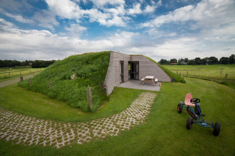 Græsdækket lodge med legecykel og picnicbord, fotograferet ved Koe in de Kost 2 i Holland.