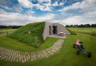 Græsdækket lodge med legecykel og picnicbord, fotograferet ved Koe in de Kost 2 i Holland.