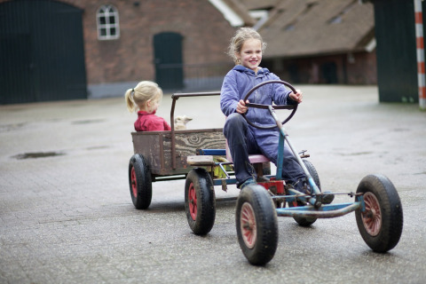 Due bambini giocano fuori in un lodge, uno guida un kart a pedali con rimorchio e l'altro siede dietro.