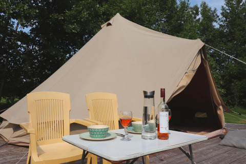 Tenda glamour 'Kreas' nei Paesi Bassi con tenda tipi, sedie gialle, tavolino, vino e alberi sullo sfondo.