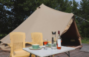 Tenda glamour 'Kreas' nei Paesi Bassi con tenda tipi, sedie gialle, tavolino, vino e alberi sullo sfondo.