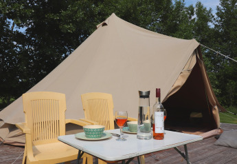 Tenda glamour 'Kreas' nei Paesi Bassi con tenda tipi, sedie gialle, tavolino, vino e alberi sullo sfondo.