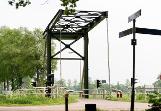 Foto van een kleine metalen brug bij een lodge, omringd door groene bomen en verkeersborden.