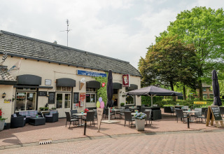 Udendørs caférestaurant med siddepladser, parasoller og grønne træer ved en hyggelig lodge.