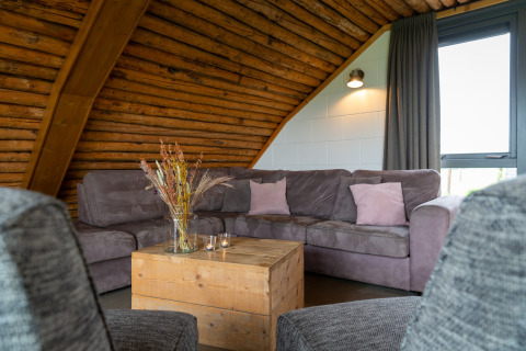 Soggiorno accogliente al lodge Koe in de Kost 3 nei Paesi Bassi con divano grigio e tavolo in legno.