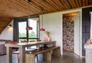 Zona pranzo in un lodge con soffitto in legno, sedute a panca, lampade rosse e carta da parati floreale.