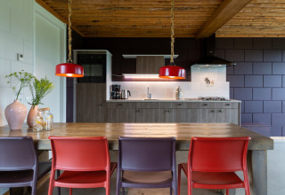 Cucina moderna di lodge con soffitto in legno, sedie colorate e lampade a sospensione rosse nei Paesi Bassi.