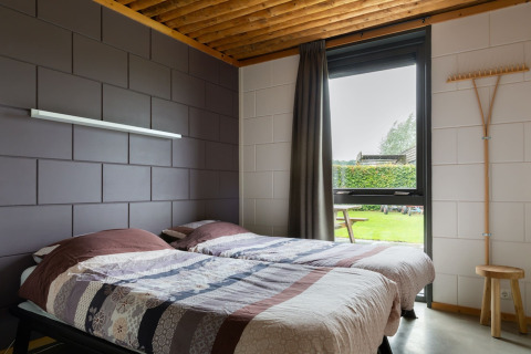 Camera con due letti singoli, arredamento moderno e finestra sul giardino nel lodge Koe in de Kost 3, Paesi Bassi.