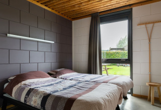 Camera con due letti singoli, arredamento moderno e finestra sul giardino nel lodge Koe in de Kost 3, Paesi Bassi.