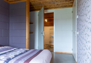 Camera da letto con pareti viola, carta da parati floreale, travi in legno e porta aperta sul bagno.