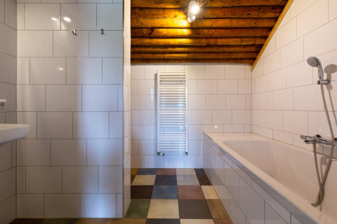 Bagno moderno con piastrelle bianche, vasca, soffitto in legno a vista e pavimento colorato.