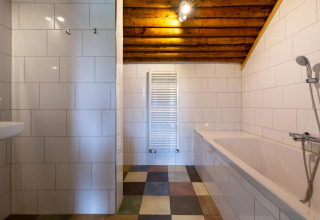 Bagno moderno con piastrelle bianche, vasca, soffitto in legno a vista e pavimento colorato.