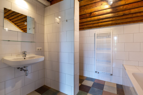 Bagno moderno di lodge con piastrelle bianche, soffitto in legno, specchio, lavabo e scalda salviette.