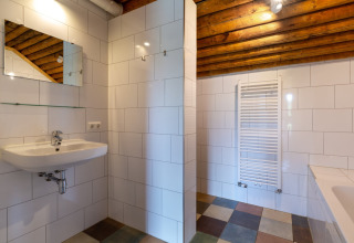 Bagno moderno di lodge con piastrelle bianche, soffitto in legno, specchio, lavabo e scalda salviette.