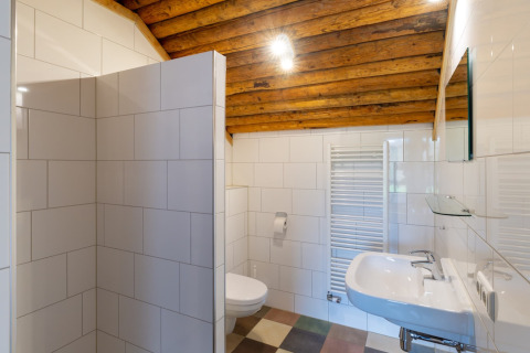Bagno con piastrelle bianche, soffitto in legno, lavabo, wc e termosifone in un lodge olandese.