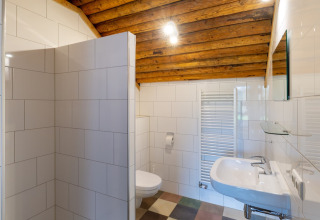 Bagno con piastrelle bianche, soffitto in legno, lavabo, wc e termosifone in un lodge olandese.