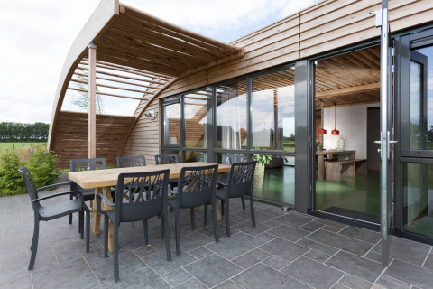 Zona pranzo esterna del lodge Koe in de Kost 3 nei Paesi Bassi con terrazza moderna in legno e vetrate.