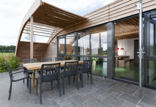 Zona pranzo esterna del lodge Koe in de Kost 3 nei Paesi Bassi con terrazza moderna in legno e vetrate.